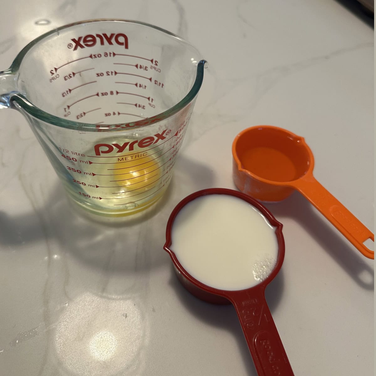 Egg in a beaker, milk and oil in measuring cups on the counter.