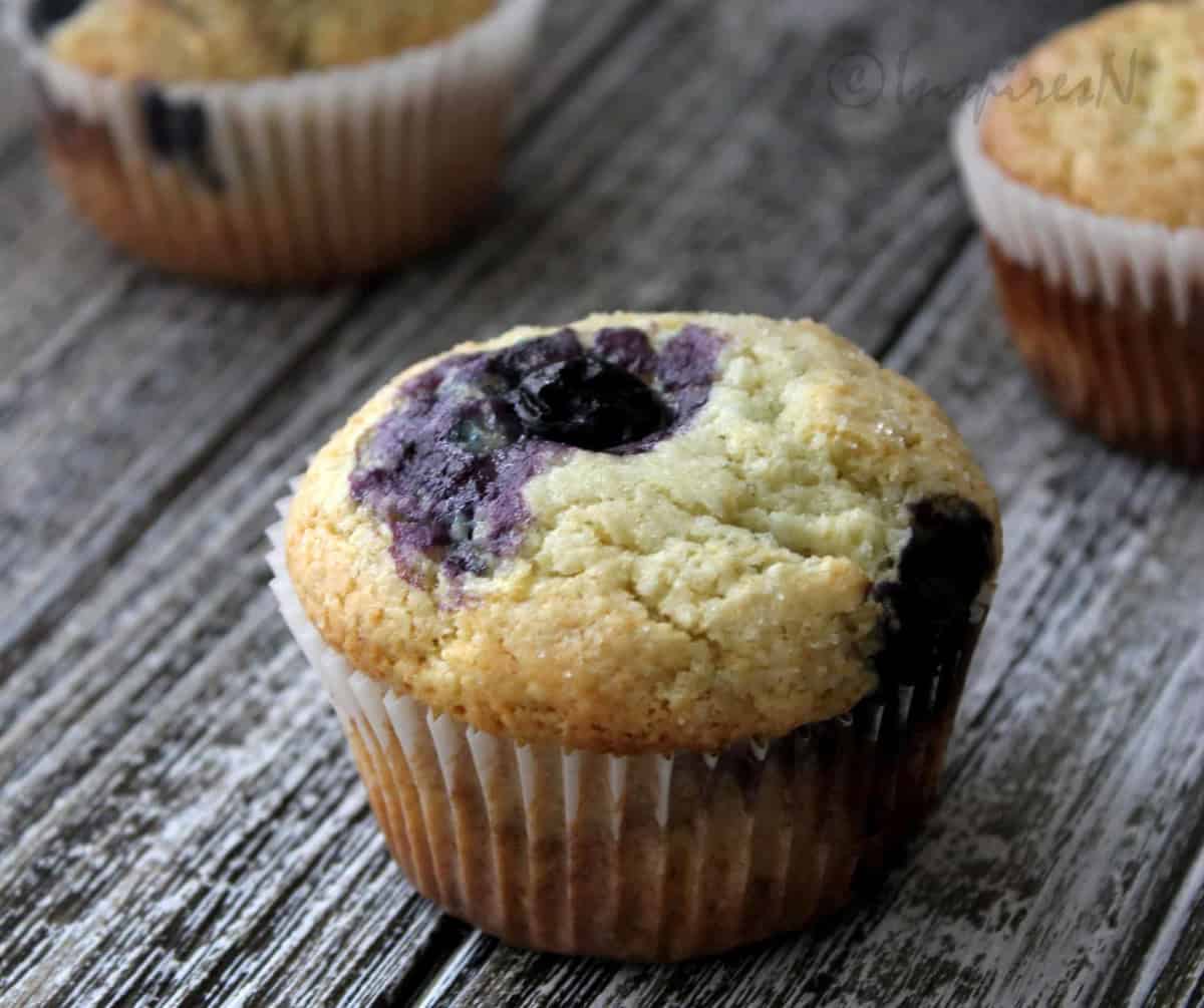 Bakery style blueberry muffins on a wooden plank.