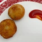 Fish cutlet served in a white plate with ketchup on the side.