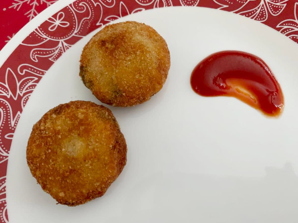Fish cutlet served in a white plate with ketchup on the side.