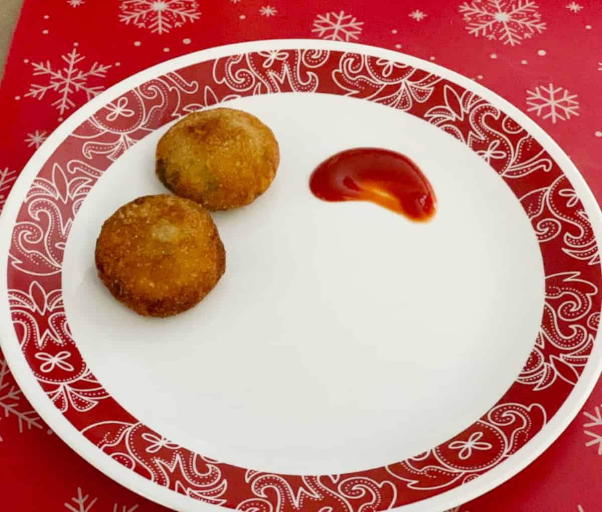 Fish cutlet served in a white plate with ketchup on the side.