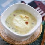 Rasmalai topped with nuts served in a white bowl.