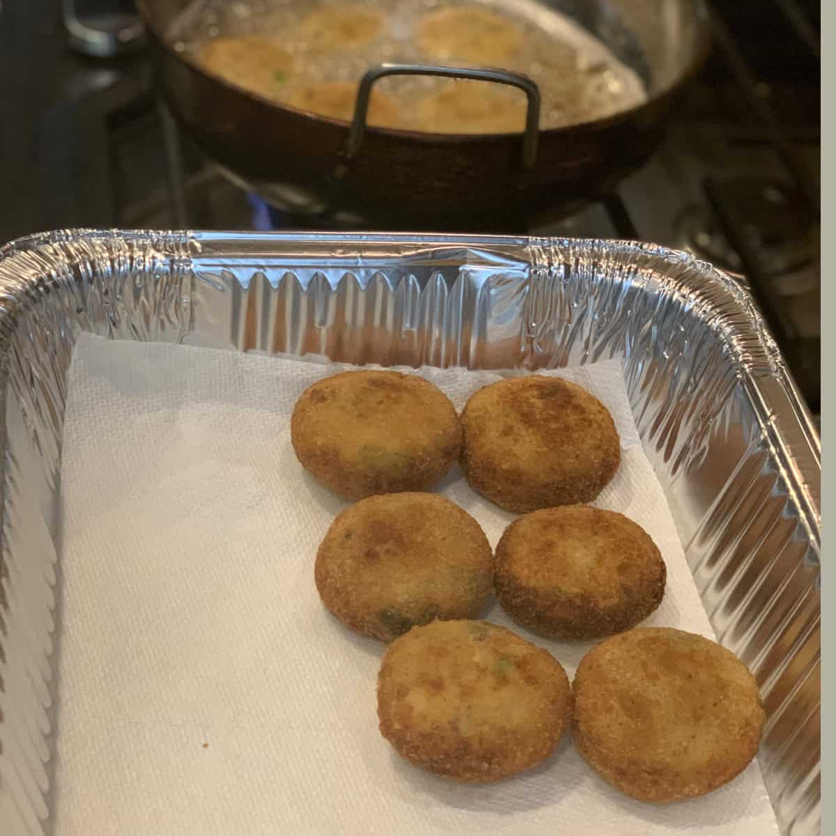 Fried fish cutlet drained onto paper towel in an aluminum tray.