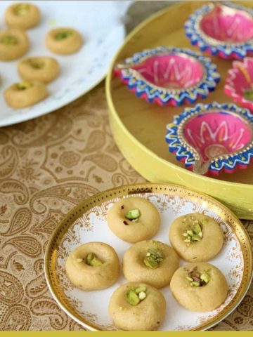 Microwave milk peda in a ceramic plate with lamps or diyas in a yellow box.
