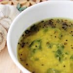 Phiki dal Lentil Soup in a white bowl with 2 garlic on a wooden board.