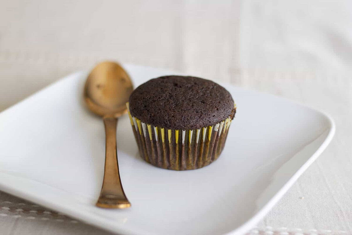 Eggless chocolate cupcake served in a white plate with a golden plated dessert spoon.