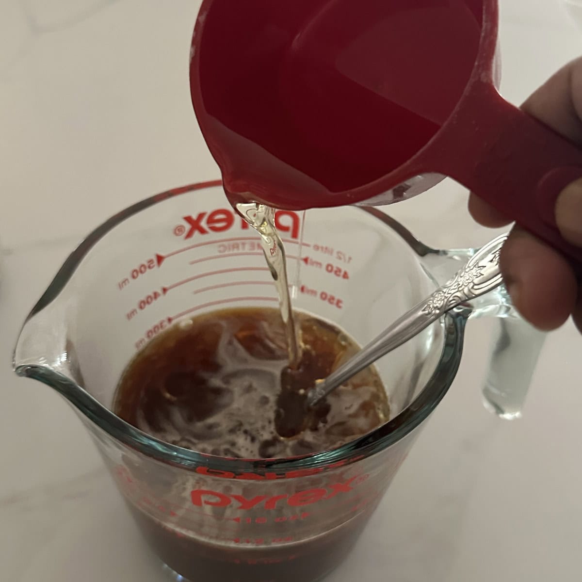 Add oil using a red cup to coffee in a glass beaker.