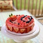 Strawberry shortcake with whipped cream frosting ready on a white cake stand.
