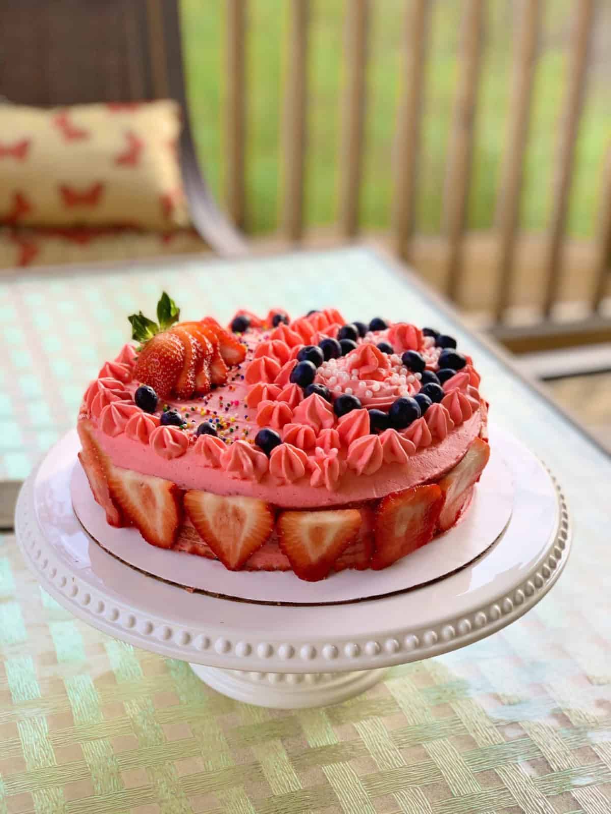 Strawberry shortcake with whipped cream frosting ready on a white cake stand.