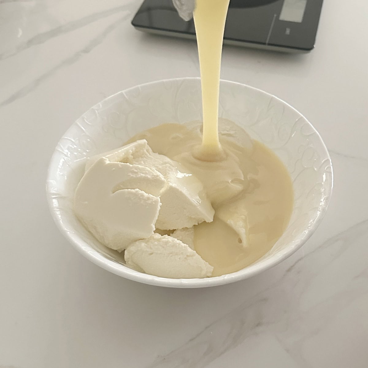 A bowl of ricotta cheese and condensed milk being poured into a bowl.