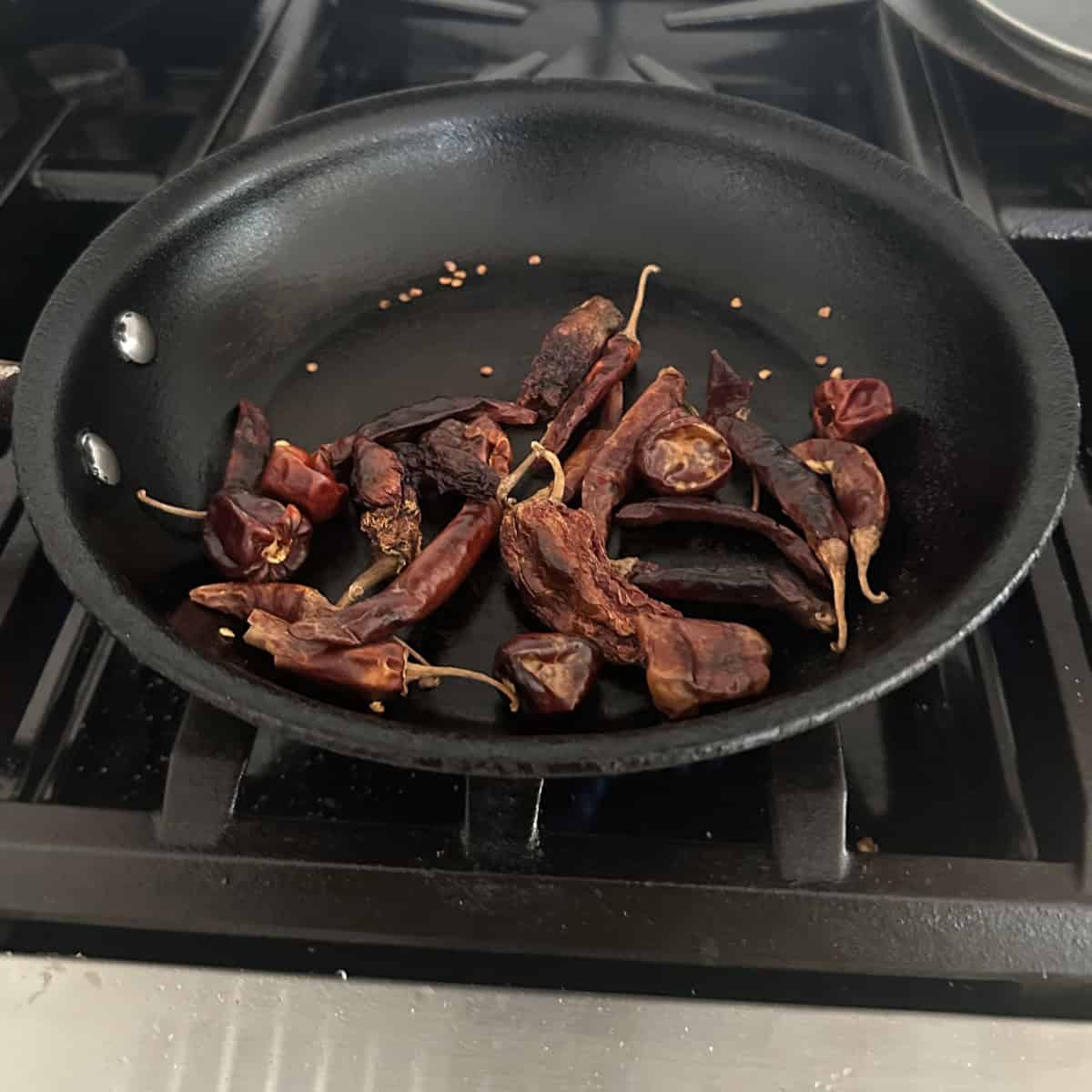 Dried red chili peppers roasting in a black non-stick skillet on a stovetop.