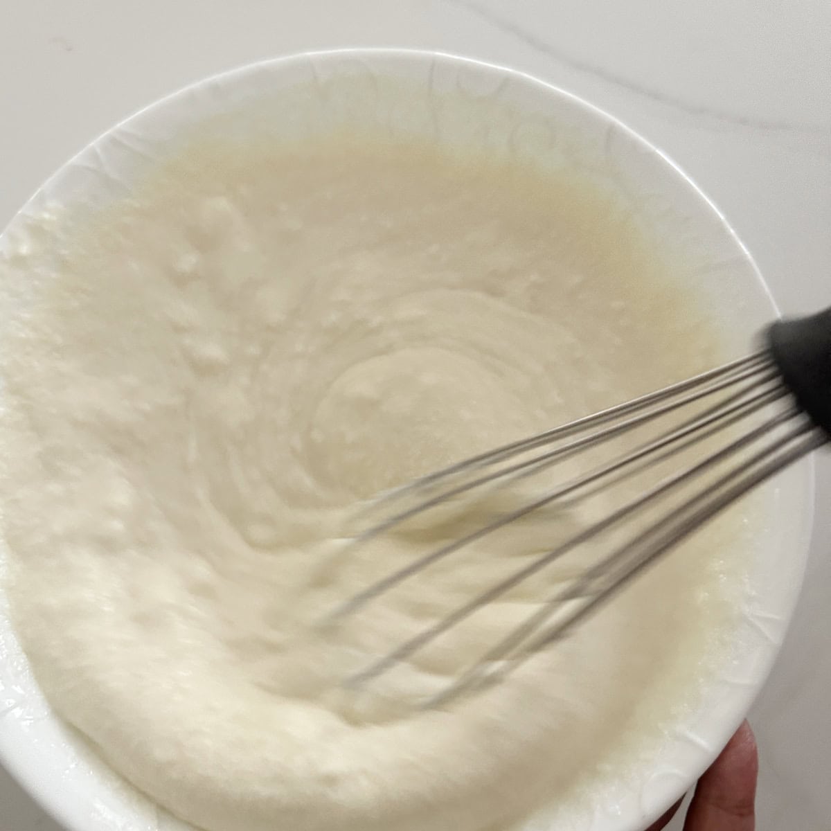 A bowl of ricotta cheese and condensed milk with a whisk in it.