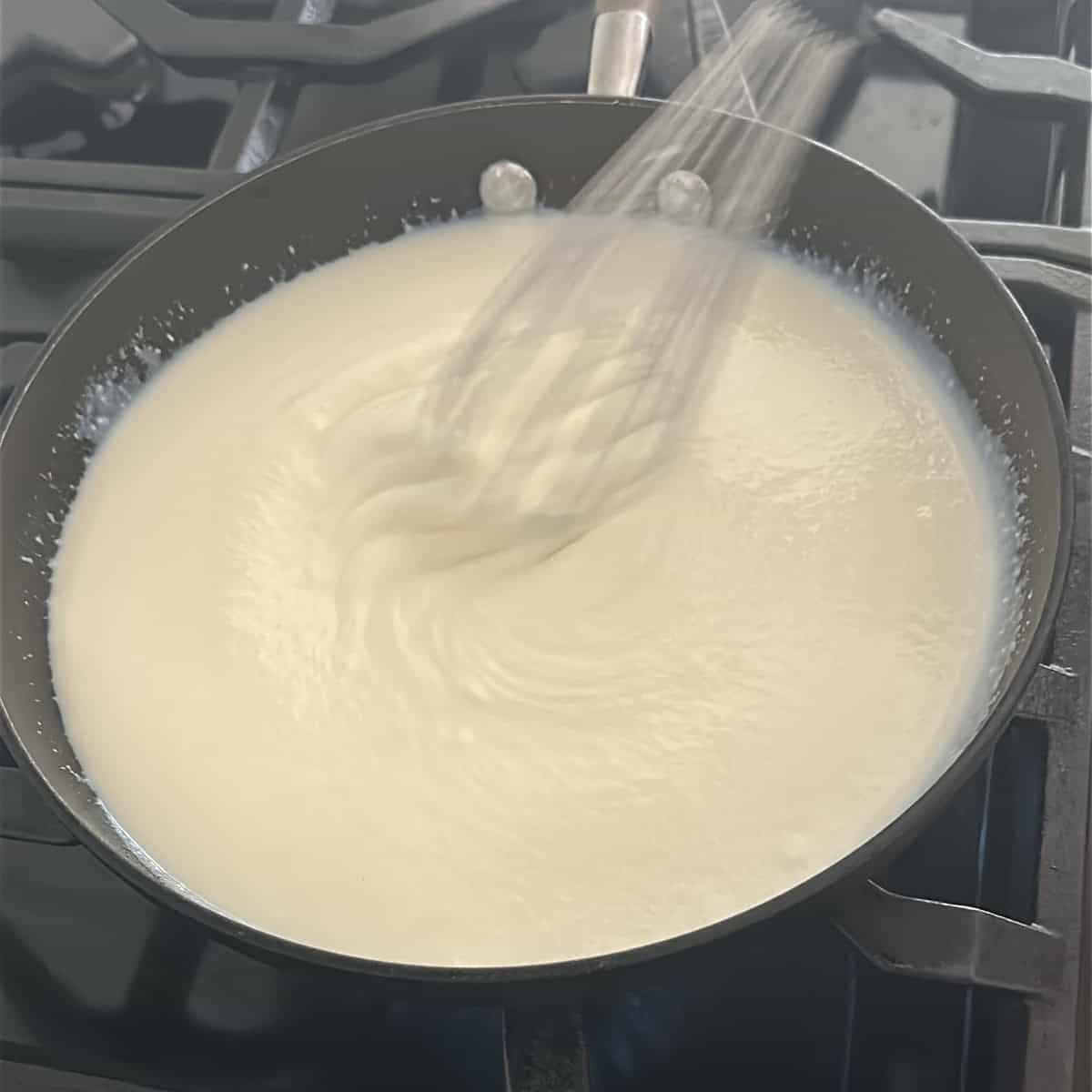 A pan with a whisk in it cooking ricotta cheese peda.