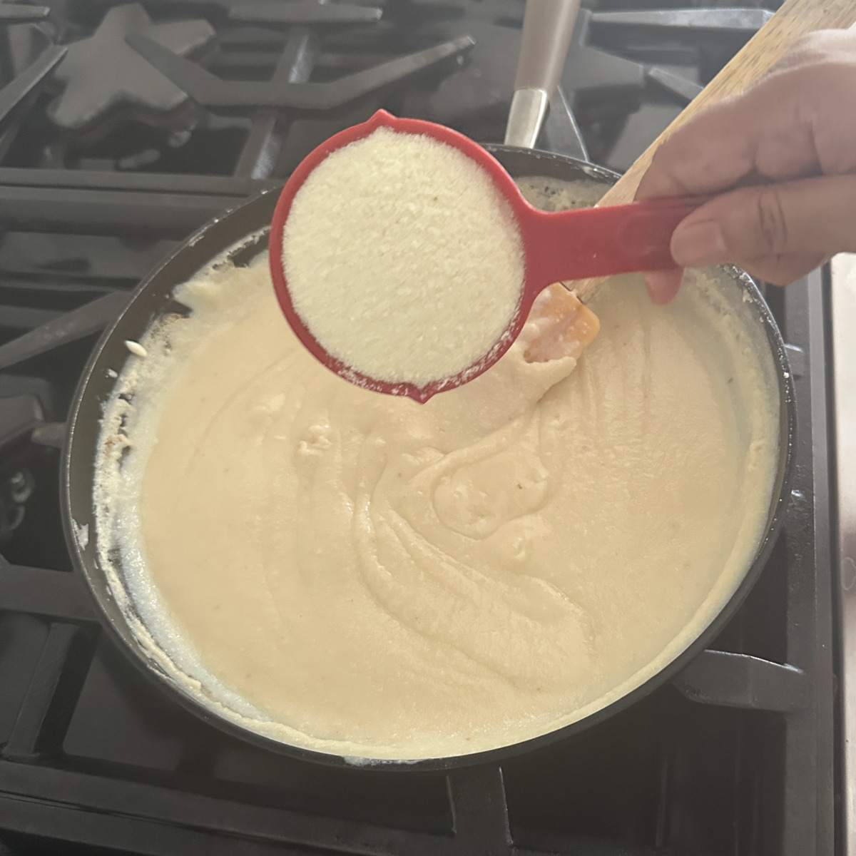 Adding milk powder to a pan with ricotta cheese on a stove.