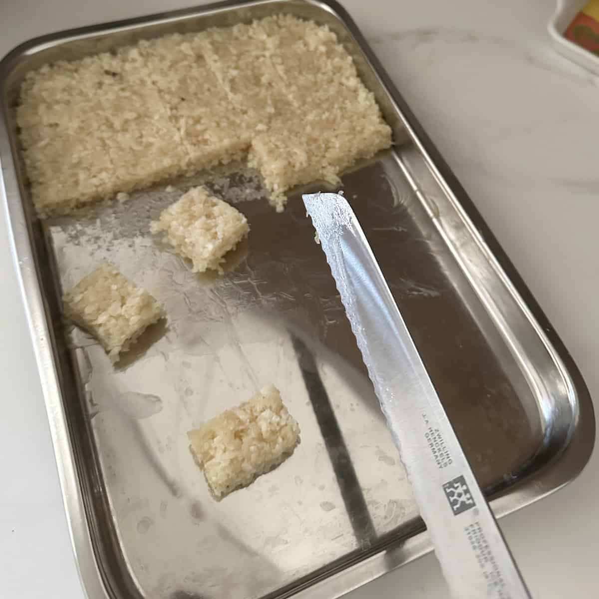 A tray with coconut burfi on it with a knife to cut onto slices.