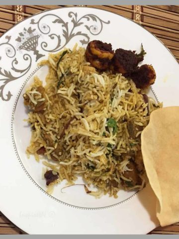 Mutton biryani served on a ceramic pate with pappad and fried shrimp made using mutton biryani easy recipe.
