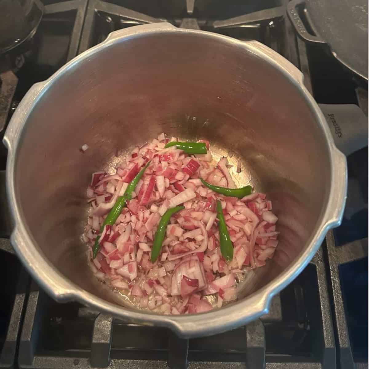 sauteeing onions, green chilies in a pressure cooker on stove top to make Rajma gravy.