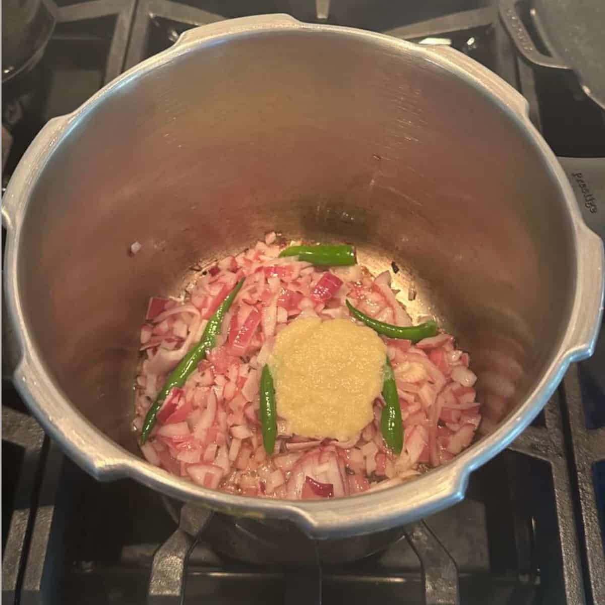 sauteeing onions, green chilies and ginger garlic paste in a pressure cooker on stove top to make Rajma gravy.