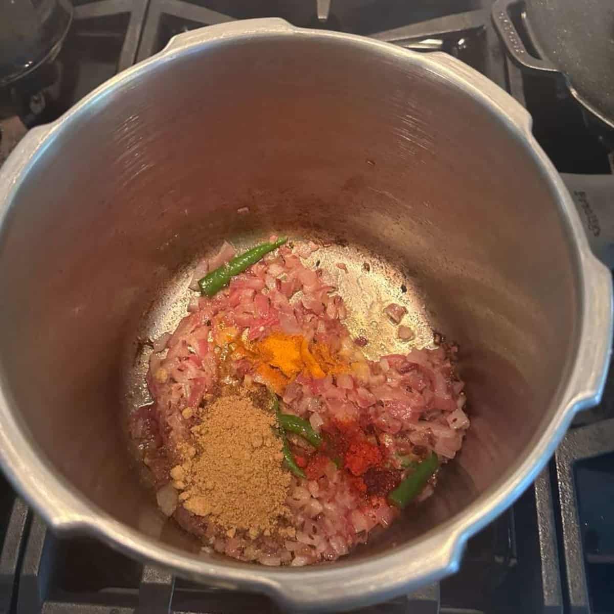 sauteeing onions, green chilies and spices in a pressure cooker on stove top to make Rajma gravy.
