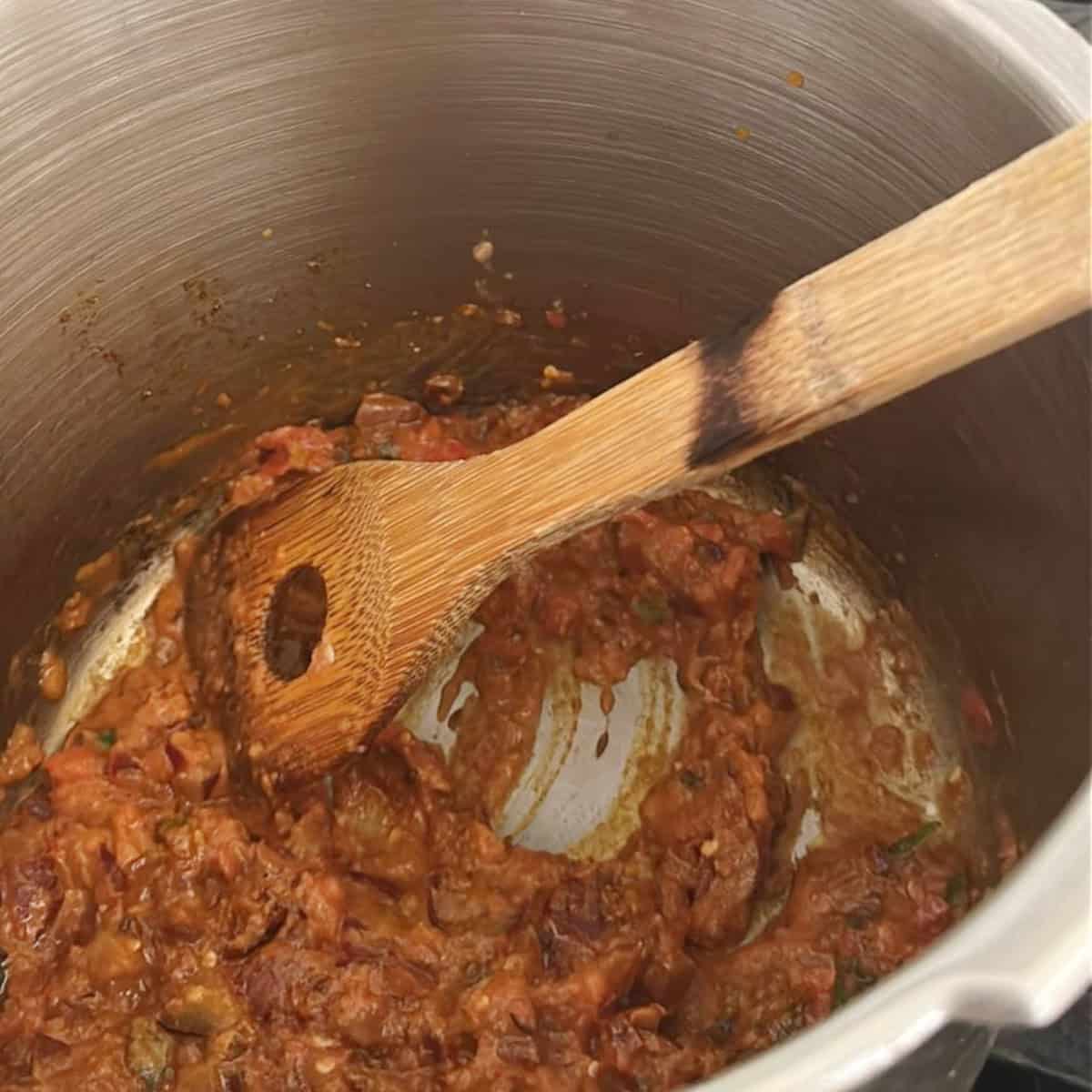 Dry Green Peas Curry base with tomatoes, onions and spices being cooked in a pressure cooker with a wooden spoon.