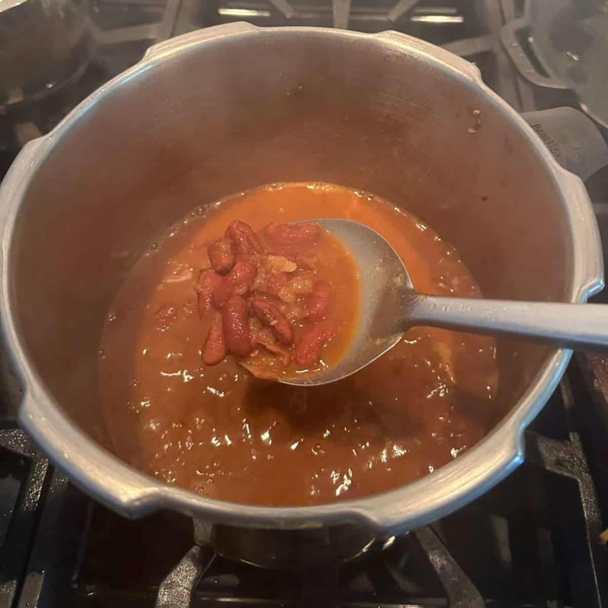 Rajma gravy in a pressure cooker being scooped with a spoon.