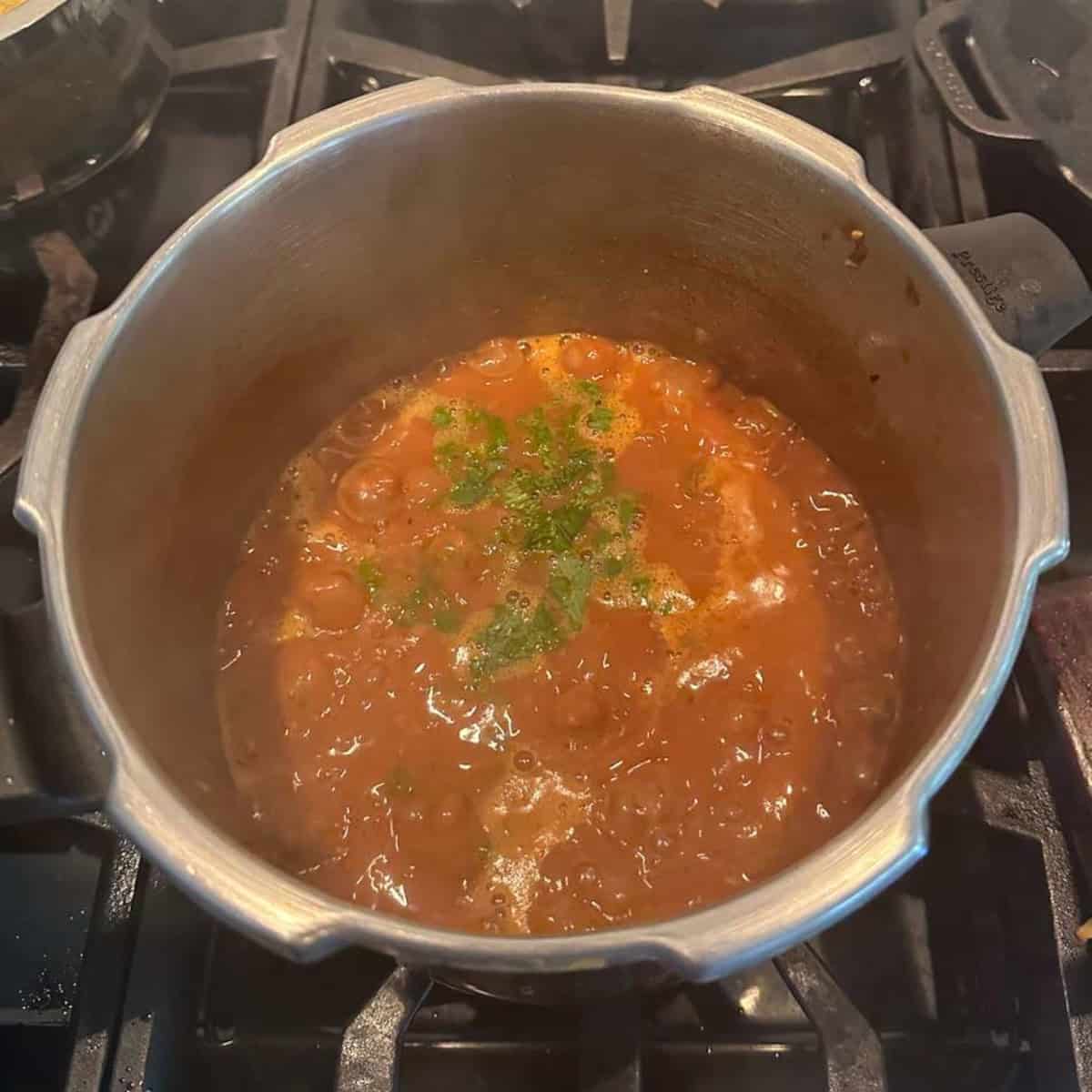 Garnish Rajma with coriander leaves in a pressure cooker cooking on a stove top.