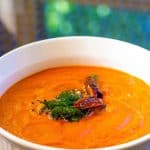 Tomato Chutney with garlic and onion served in a white container tempered with curry leaves, mustard and red chilies.