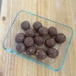 Dates and nuts ladoo in a rectangular pyrex container on a wooden counter.