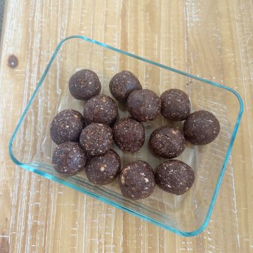 Dates and nuts ladoo in a rectangular pyrex container on a wooden counter.