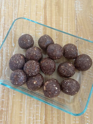 Dates and nuts ladoo in a rectangular pyrex container on a wooden counter.