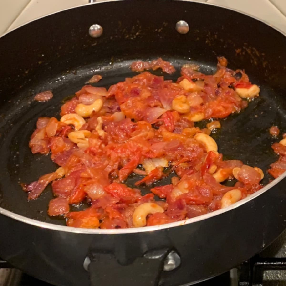 Sautee tomatoes, onions , ginger, garlic and cashew in a black pan to make Chicken Tikka masala.