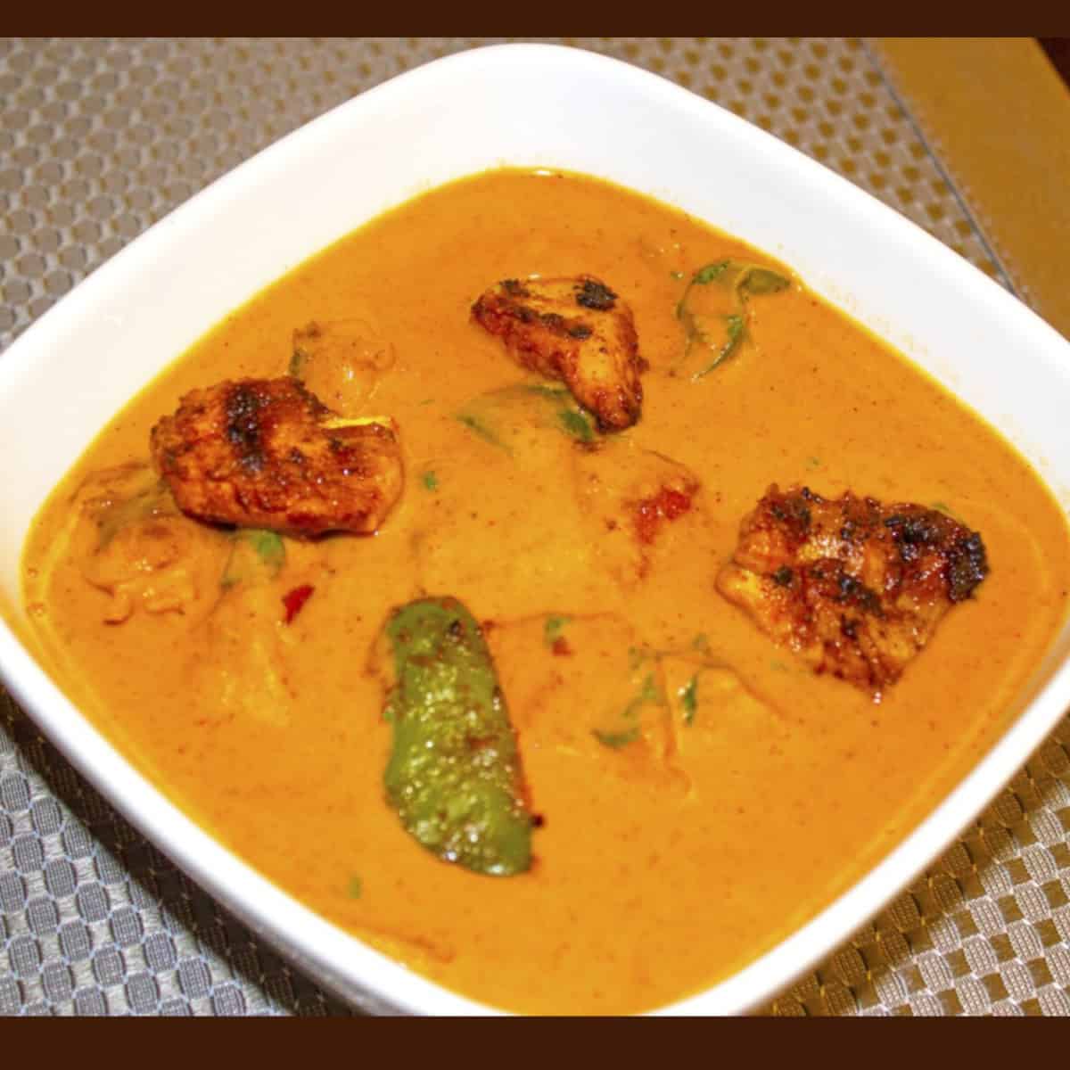 chicken tikka masala gravy served in a white bowl on a gray mat.