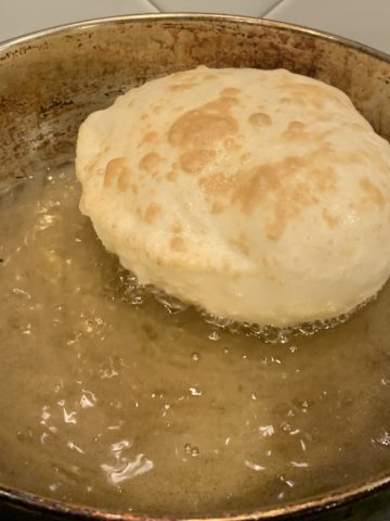 bhatura bread being deep-fried in oil in a steel wok.