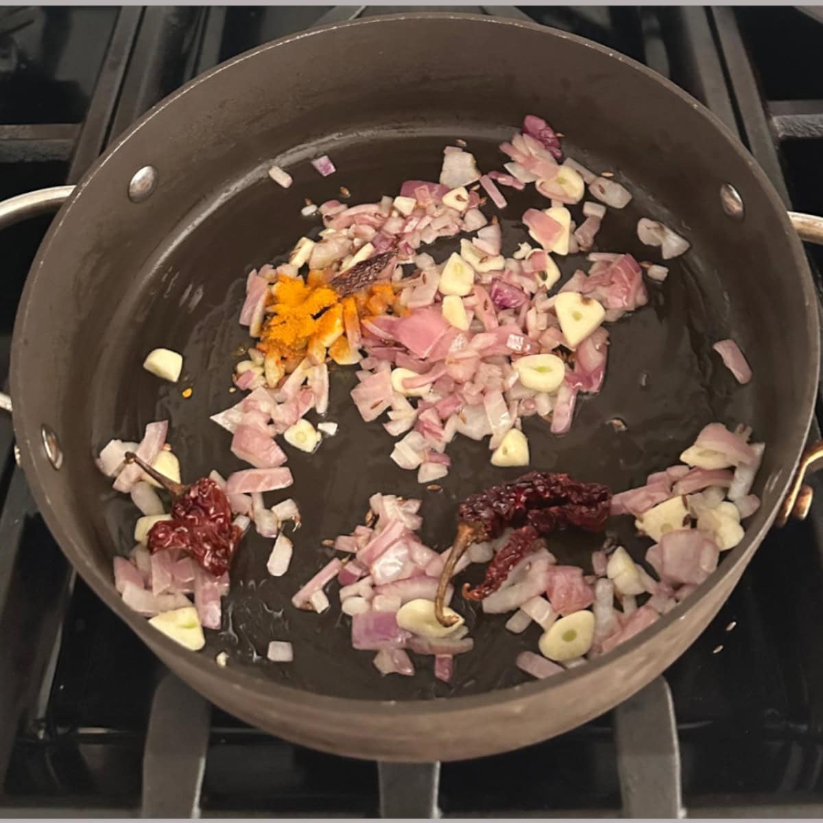 sautee onions, garlic, and red chili with turmeric in a black pan.