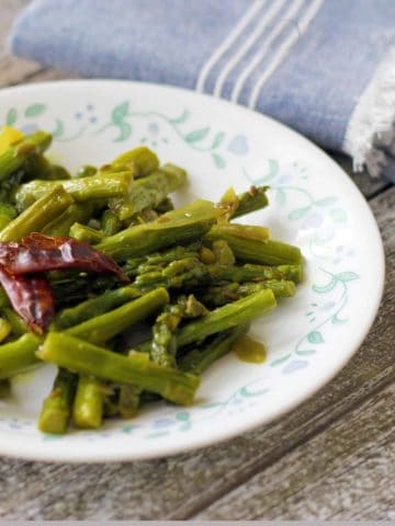 Asparagus sir fry served on a white plate and wooden board with a blue kitchen towel next to it .