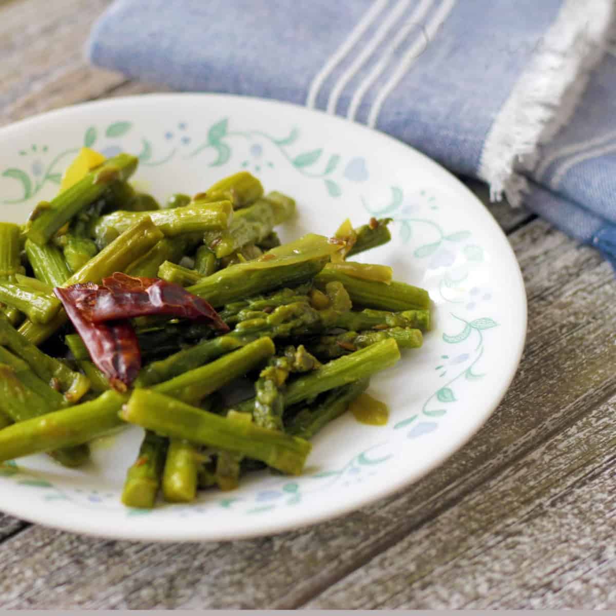 Asparagus sir fry served on a white plate and wooden board with a blue kitchen towel next to it .