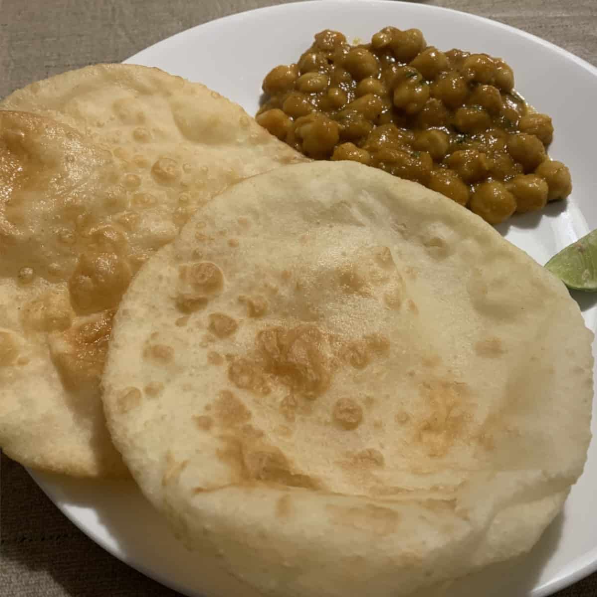 Bhatura Bread with chana masala in a white plate with a lemon wedge.