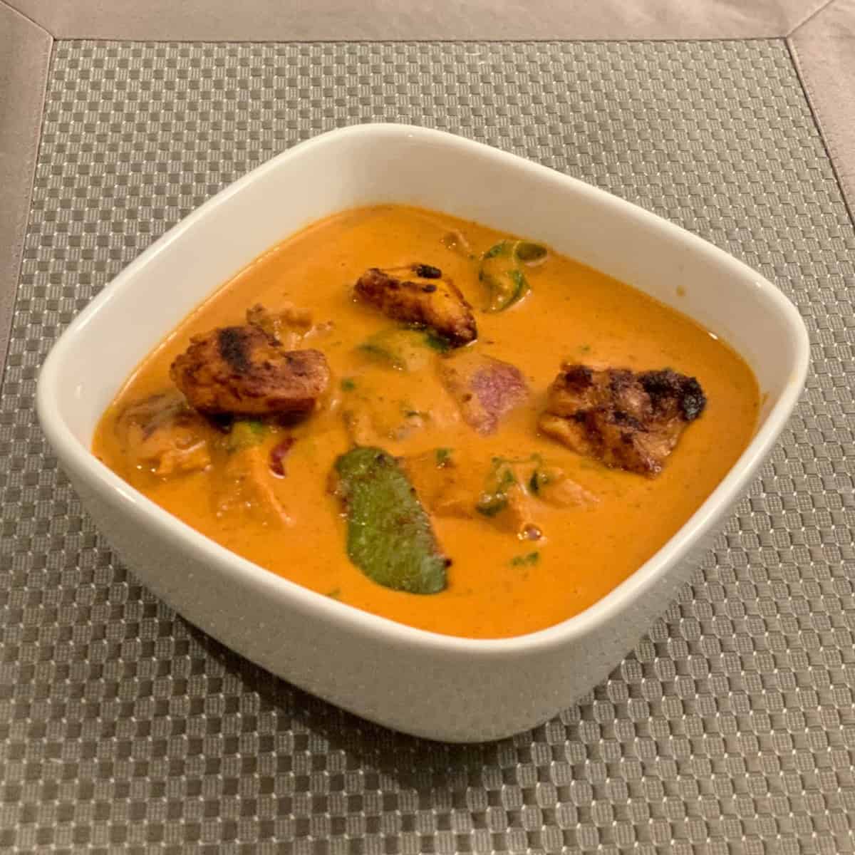 chicken tikka masala gravy served in a white bowl on a gray mat.