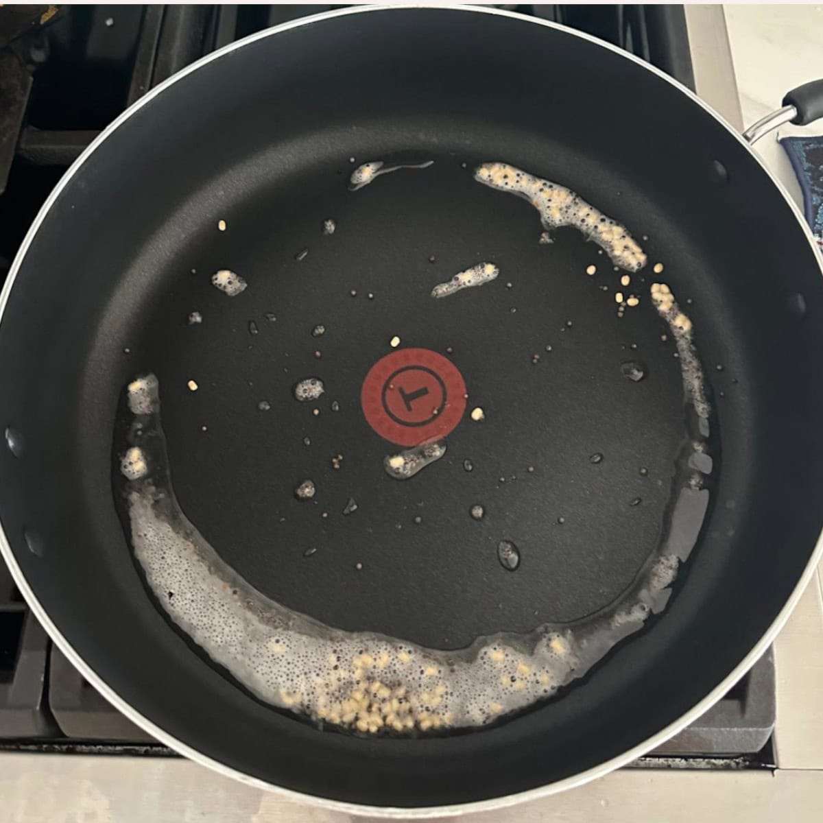 Cabbage coconut stir fry preparation with spluttering mustard and urad in oil in a black pan on stove top.