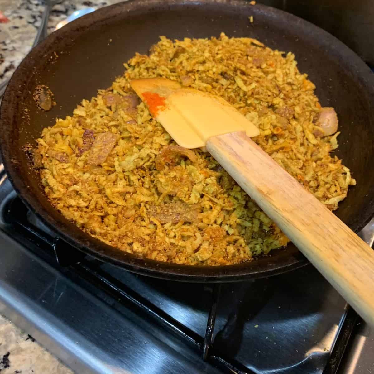 roasting the coconut with spices in a black pan with a wooden ladle.