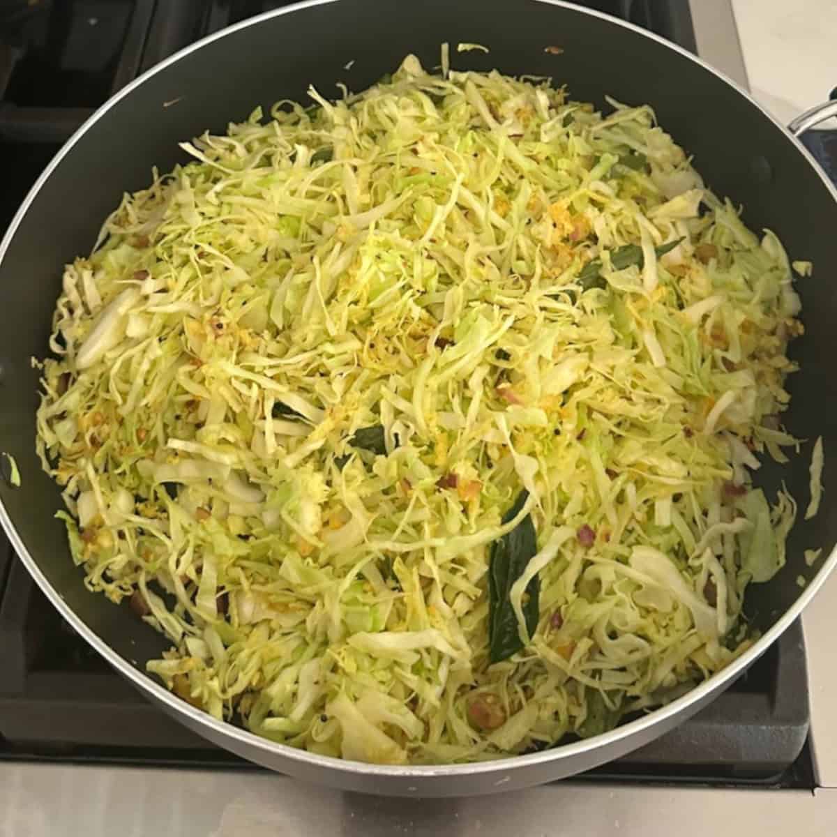 cabbage stir fry preparation in a black pan on stove top.