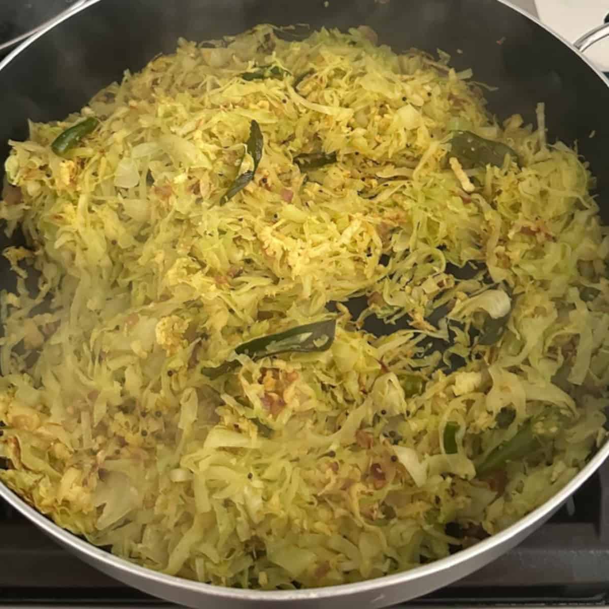 cabbage stir fry preparation in a black pan on stove top.