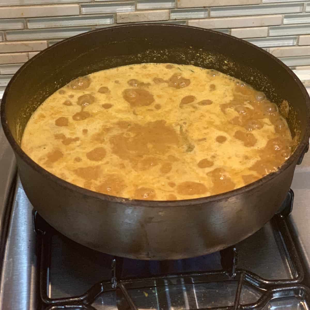 curry cooking in a black pan on gas stove.