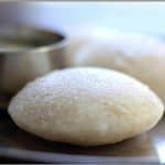 Soft Idli served with a bowl of chutney on the side.