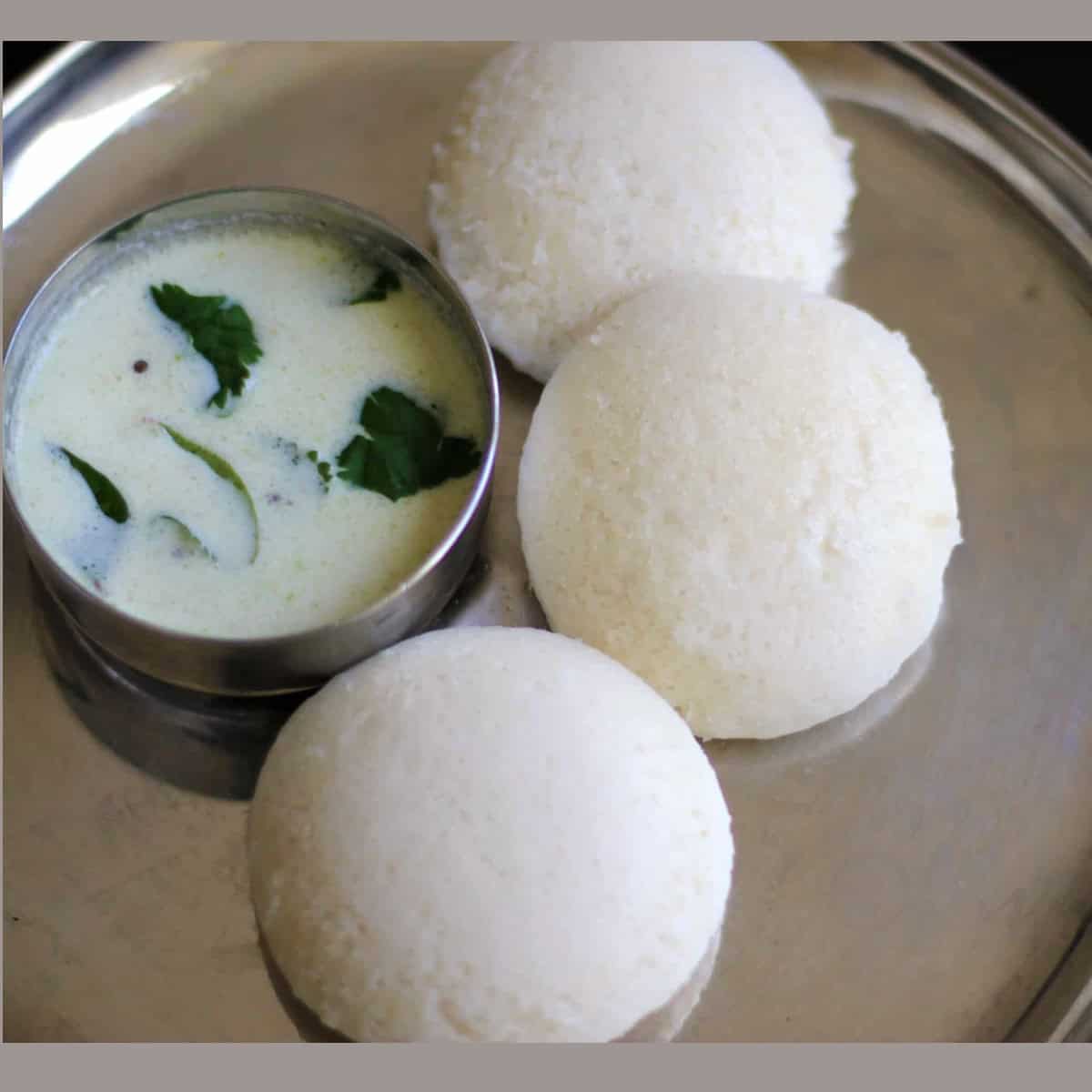 Idli served on a steel plate with chutney on the side.