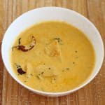 Mambazha Pulisseri ripe mango curry served in a white bowl on a wooden board.