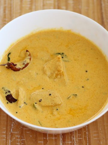 Mambazha Pulisseri ripe mango curry served in a white bowl on a wooden board.