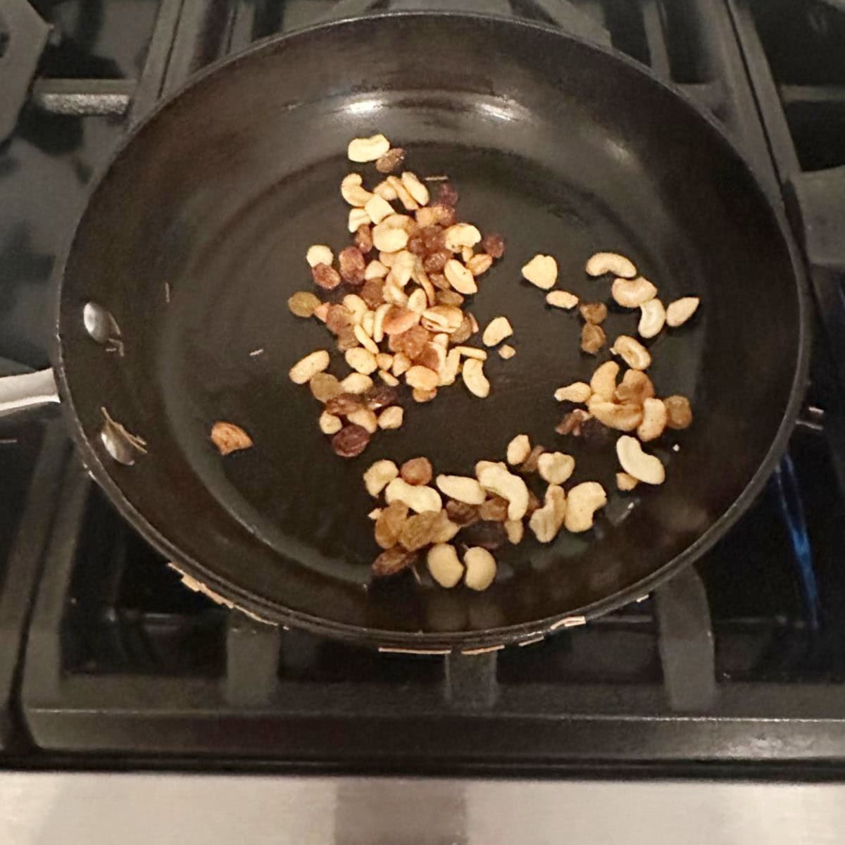 frying nuts and raisins in a black pan.