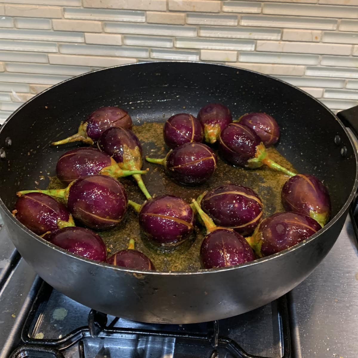 spiced slit eggplant sauteed in a black pan.