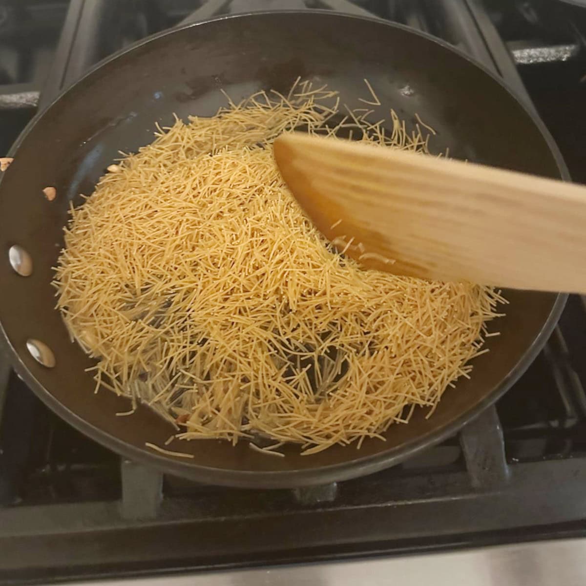 Roasting vermicelli in ghee in a black pan with a wooden spatula.